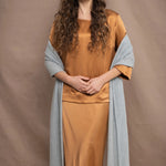 a woman wears a large cashmere wrap shawl in light pale blue turquoise over bronze silk clothing top and skirt