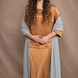a woman wears a large cashmere wrap shawl in light pale blue turquoise over bronze silk clothing top and skirt