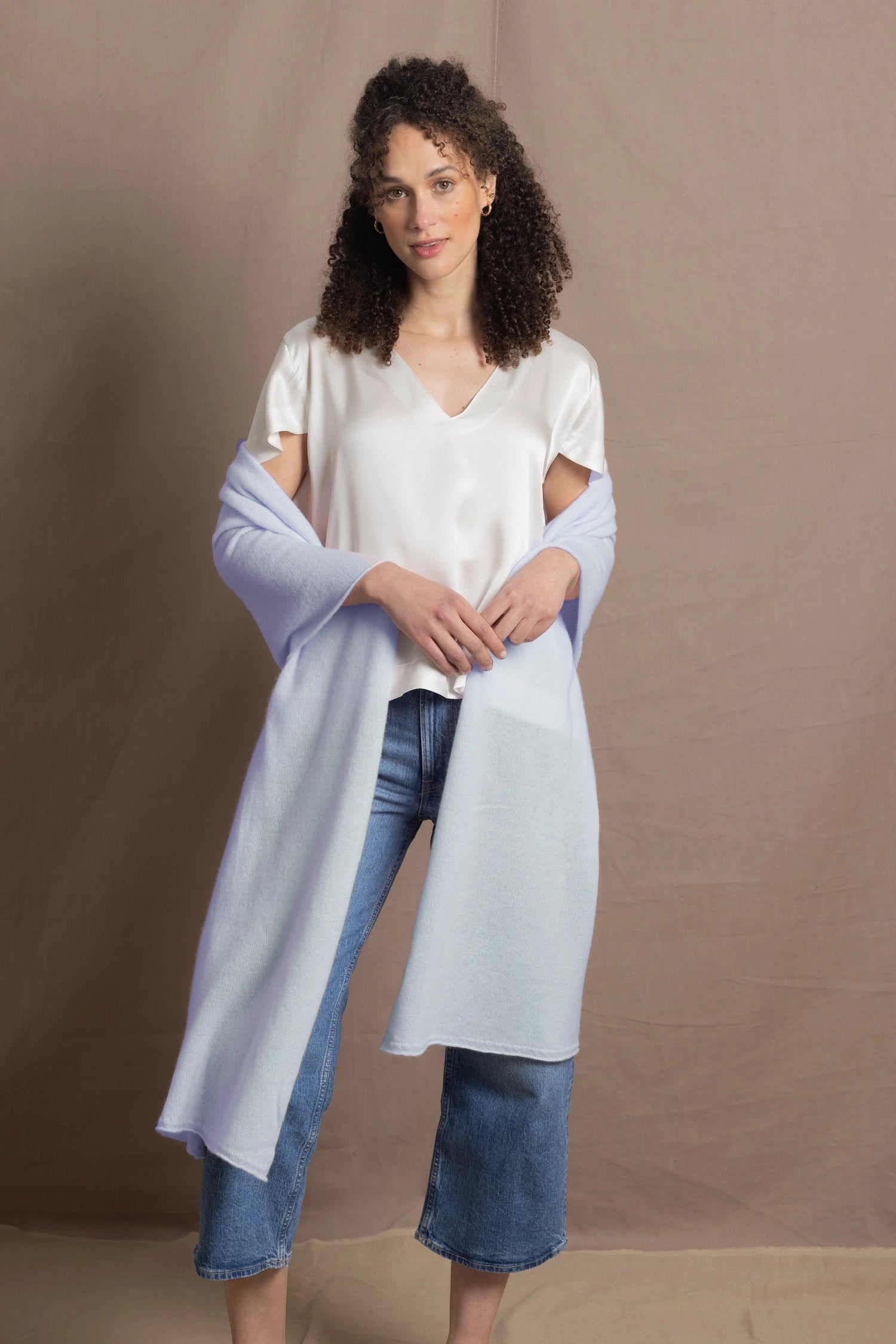 a woman wears a pale blue cashmere wrap shawl over her shoulders with a silk white tee and jeans