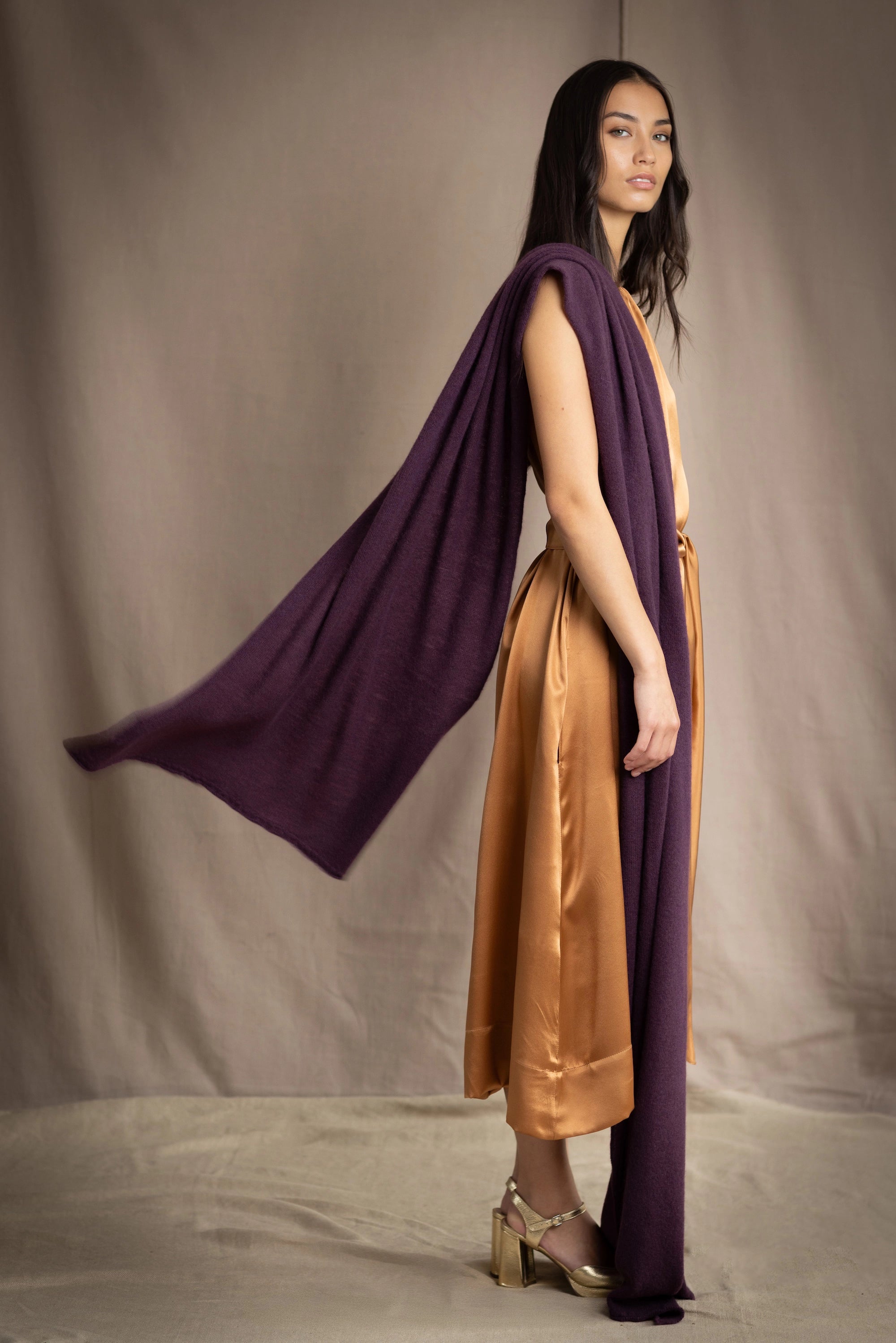 a woman wearing a large cashmere wrap shawl in dark purple over a bronze silk dress