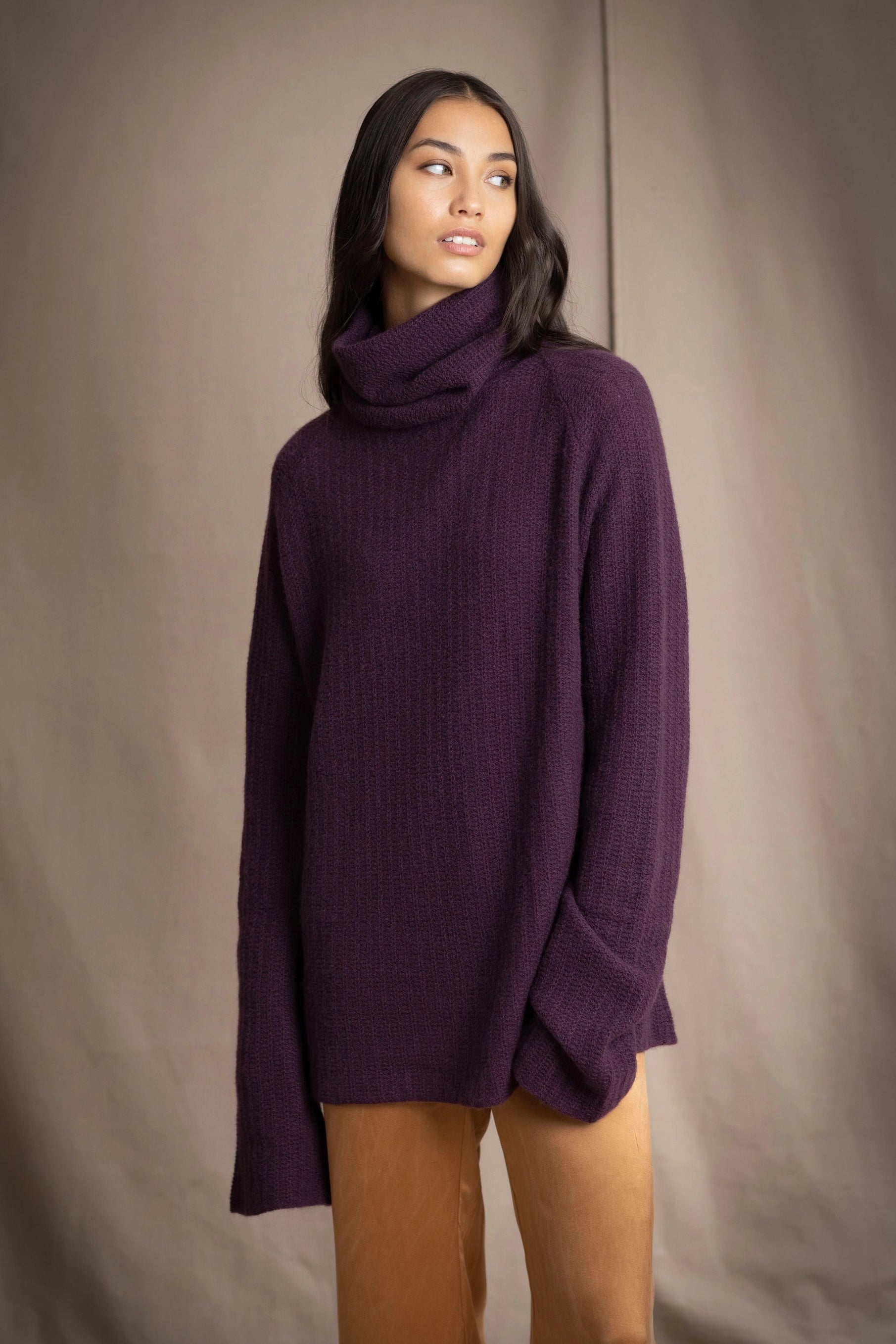 Woman wearing a cashmere fisherman turtleneck sweater in dark purple with bronze silk trousers