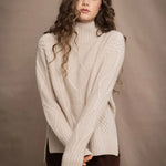 A woman wears a hand knit Irish 100% Cashmere Aran Sweater with Turtleneck in cream beige colour