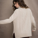A woman wears a hand knit Irish 100% Cashmere Aran Sweater with Turtleneck in cream beige colour