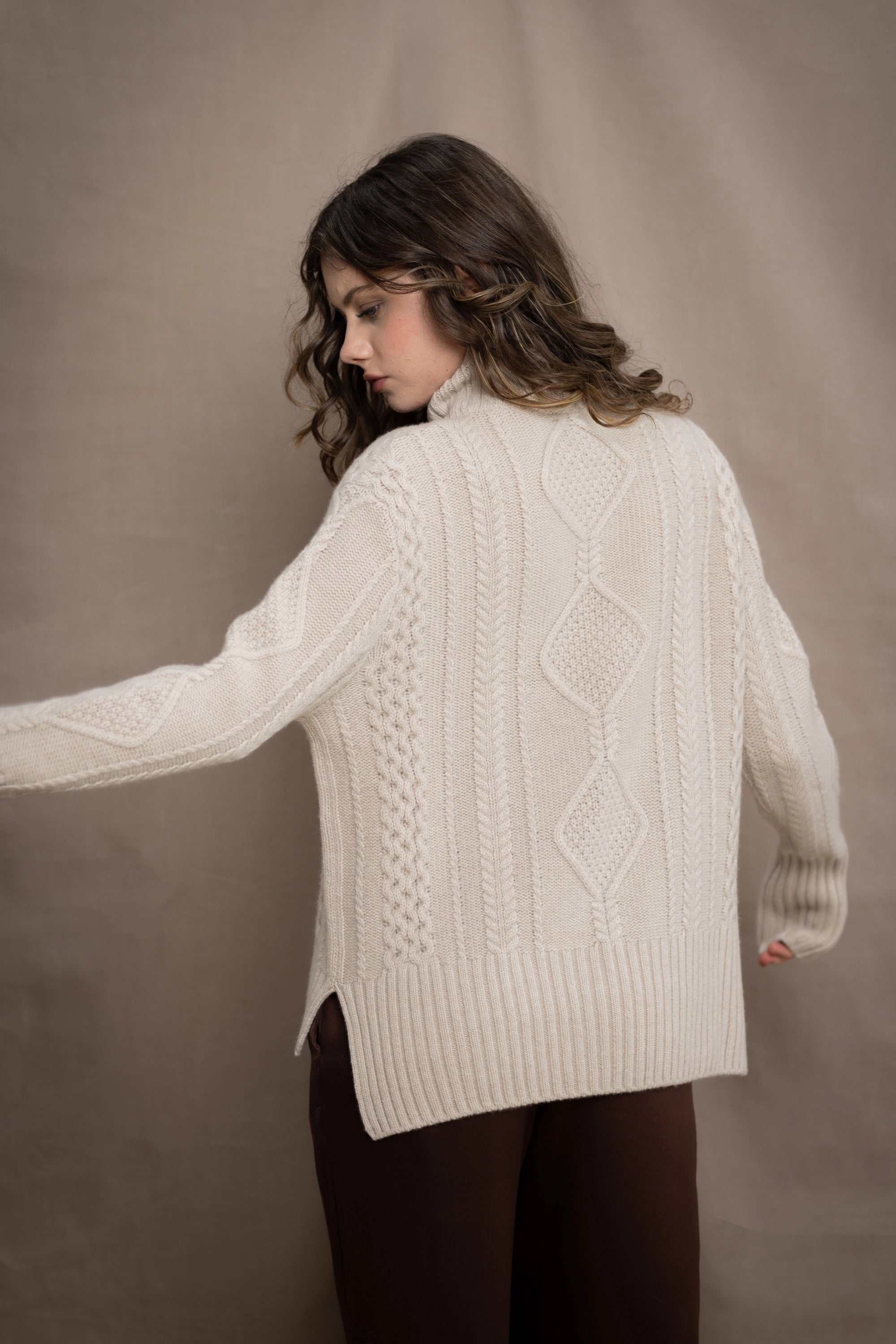 A woman wears a hand knit Irish 100% Cashmere Aran Sweater with Turtleneck in cream beige colour