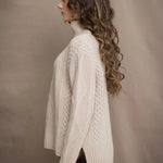A woman wears a hand knit Irish 100% Cashmere Aran Sweater with Turtleneck in cream beige colour