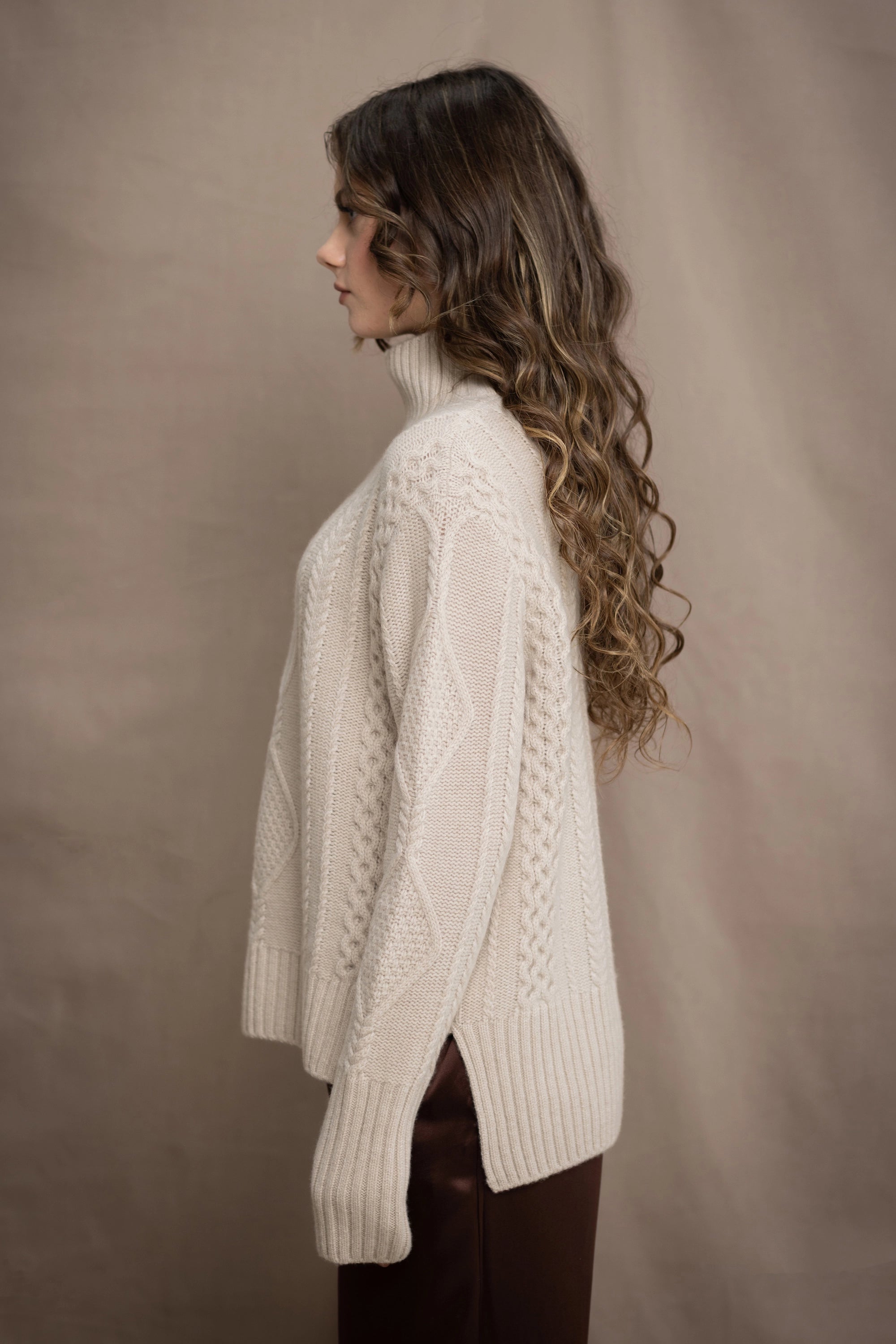 A woman wears a hand knit Irish 100% Cashmere Aran Sweater with Turtleneck in cream beige colour