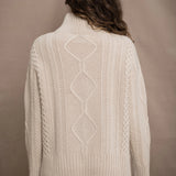 A woman wears a hand knit Irish 100% Cashmere Aran Sweater with Turtleneck in cream beige colour