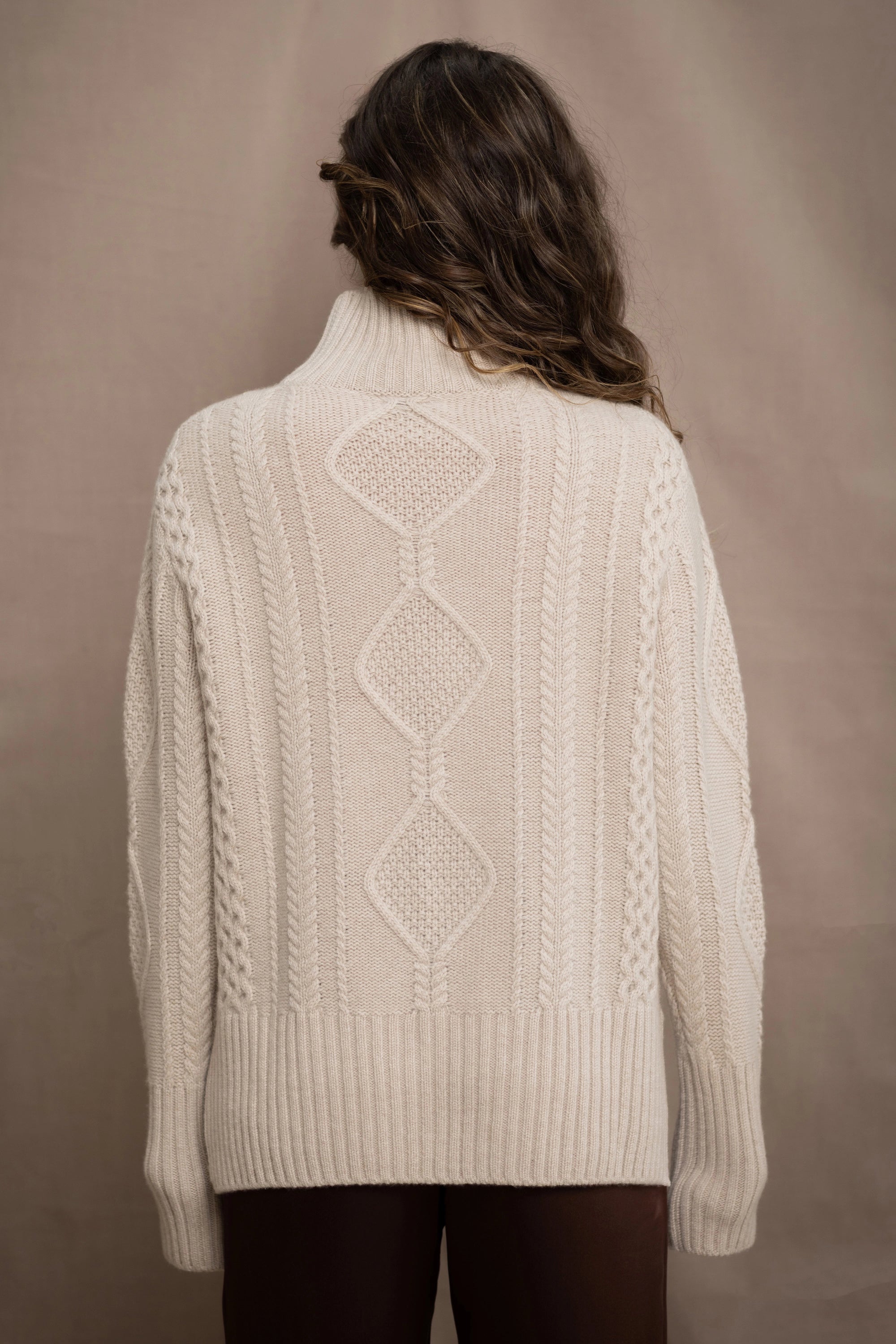 A woman wears a hand knit Irish 100% Cashmere Aran Sweater with Turtleneck in cream beige colour