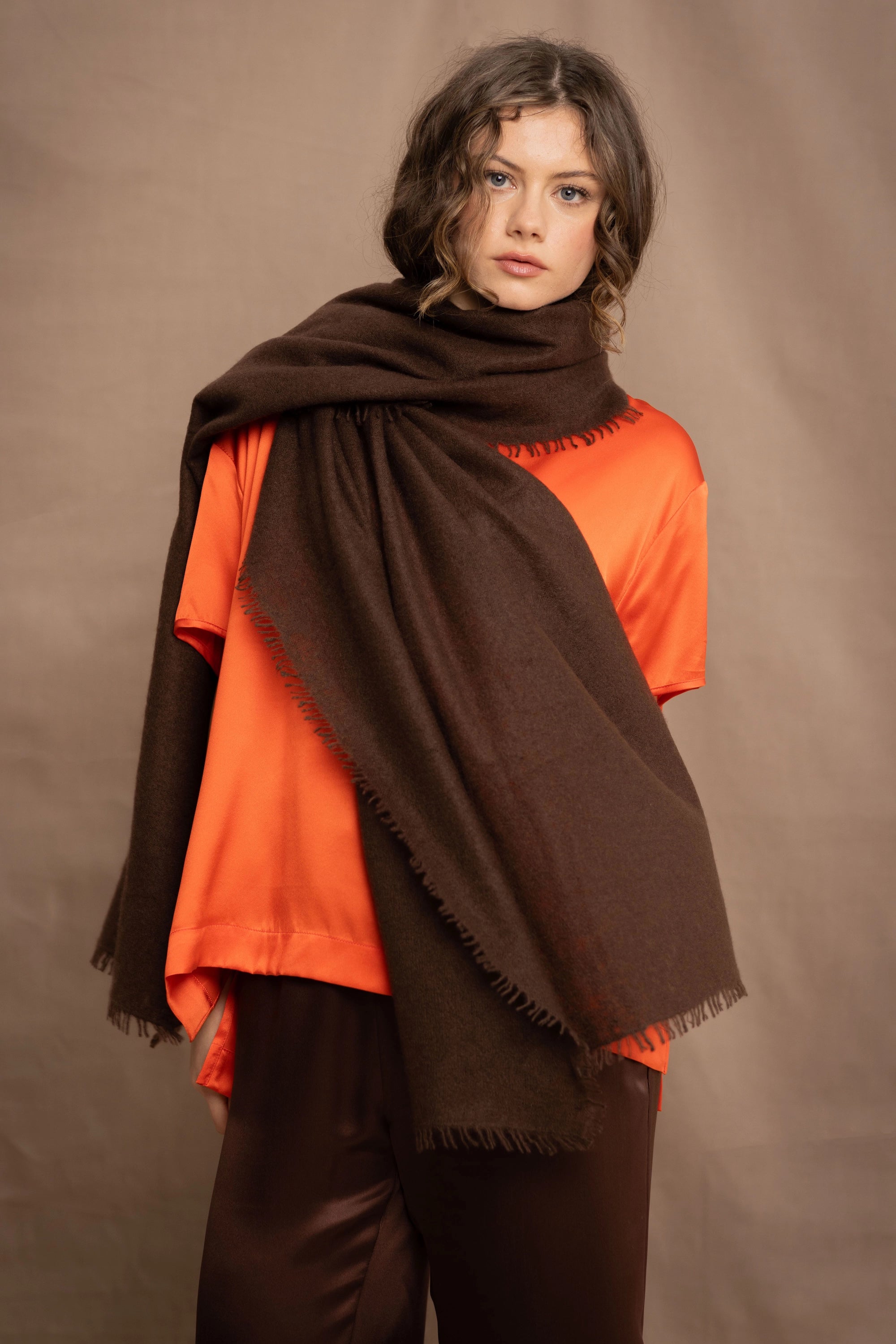 a woman wearing a lightweight cashmere wrap shawl in chocolate brown over a silk tee in bright orange and chocolate brown silk trousers