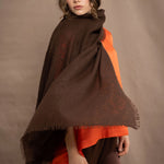a woman wearing a lightweight cashmere wrap shawl in chocolate brown over a silk tee in bright orange and chocolate brown silk trousers
