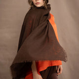 a woman wearing a lightweight cashmere wrap shawl in chocolate brown over a silk tee in bright orange and chocolate brown silk trousers