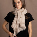A woman wears a lightweight, fine cashmere wrap scarf tied around her neck with a black cashmere t-shirt underneath