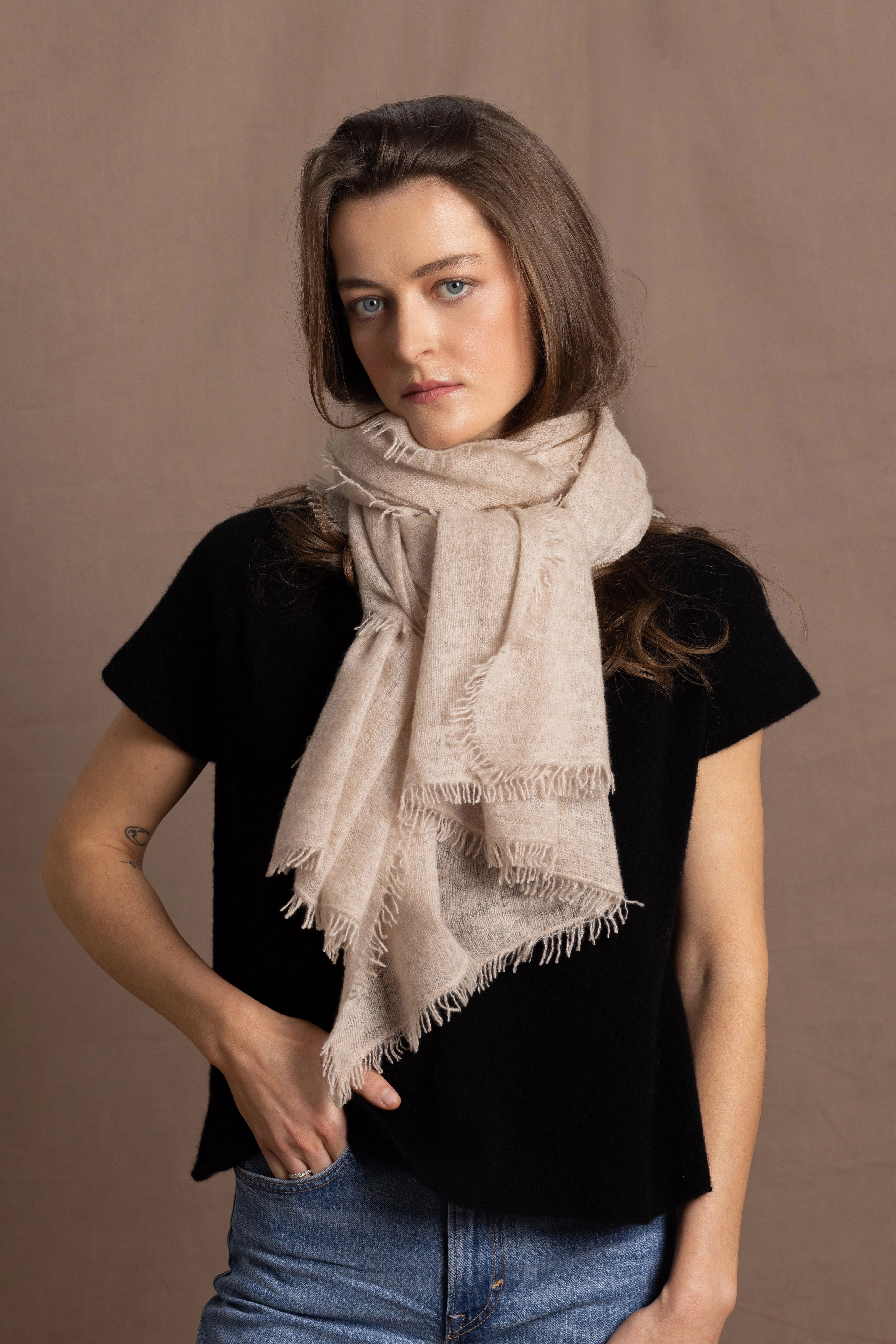 A woman wears a lightweight, fine cashmere wrap scarf tied around her neck with a black cashmere t-shirt underneath