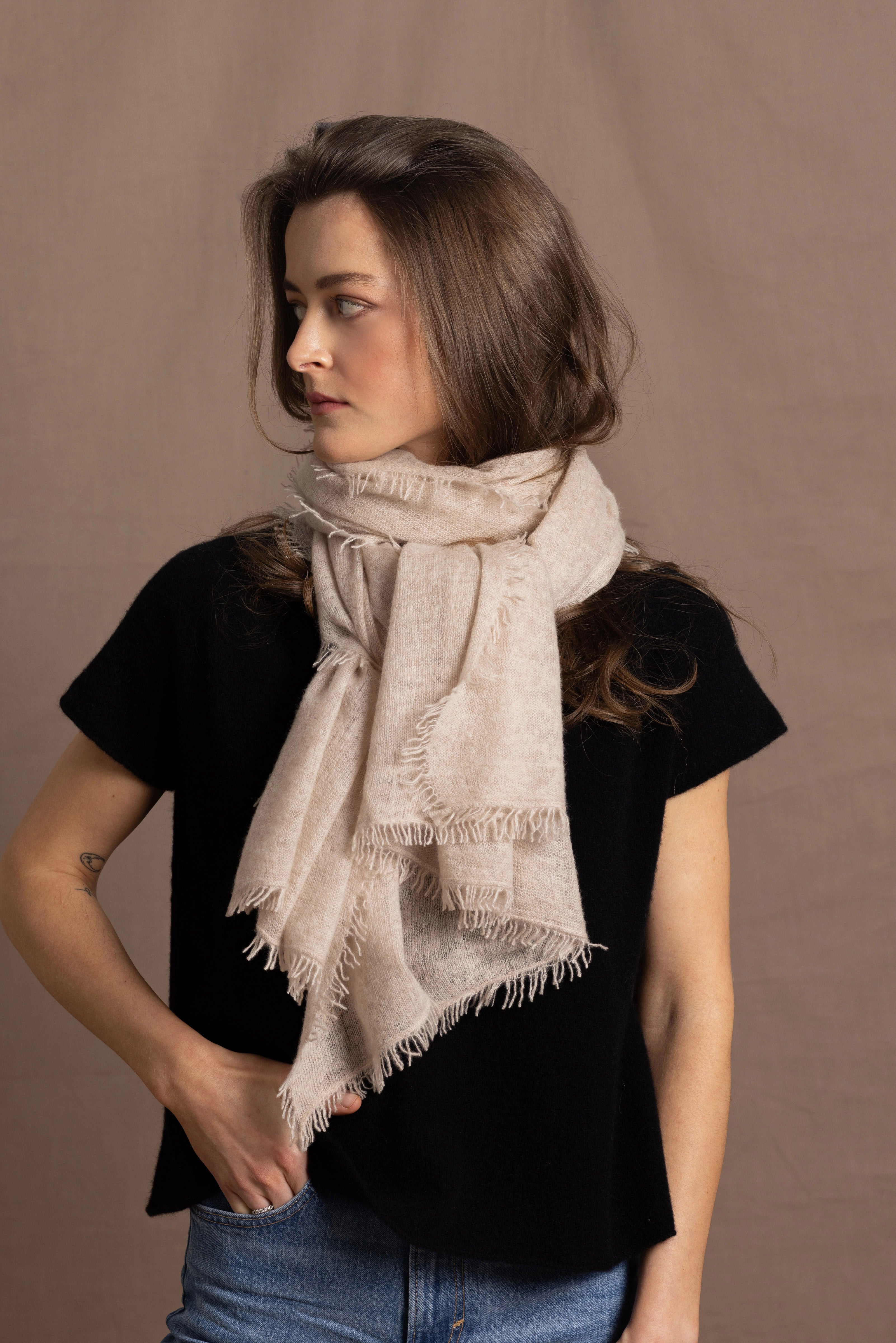 A woman wears a lightweight, fine cashmere wrap scarf tied around her neck with a black cashmere t-shirt underneath