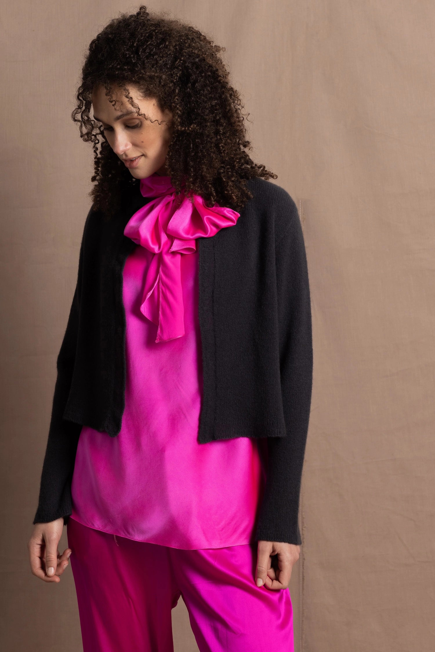 A woman wears a 100% cashmere cropped cardigan on top in navy blue over a 100% pure silk top in bright shocking pink over matching trousers 