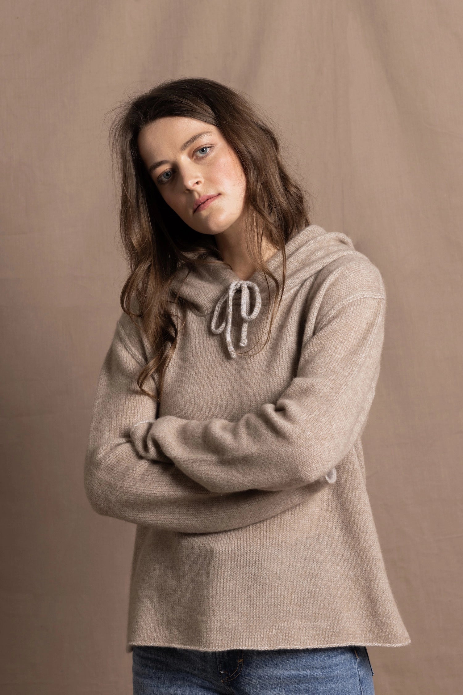a woman wears a luxury cashmere hoodie sweater in beige with jeans