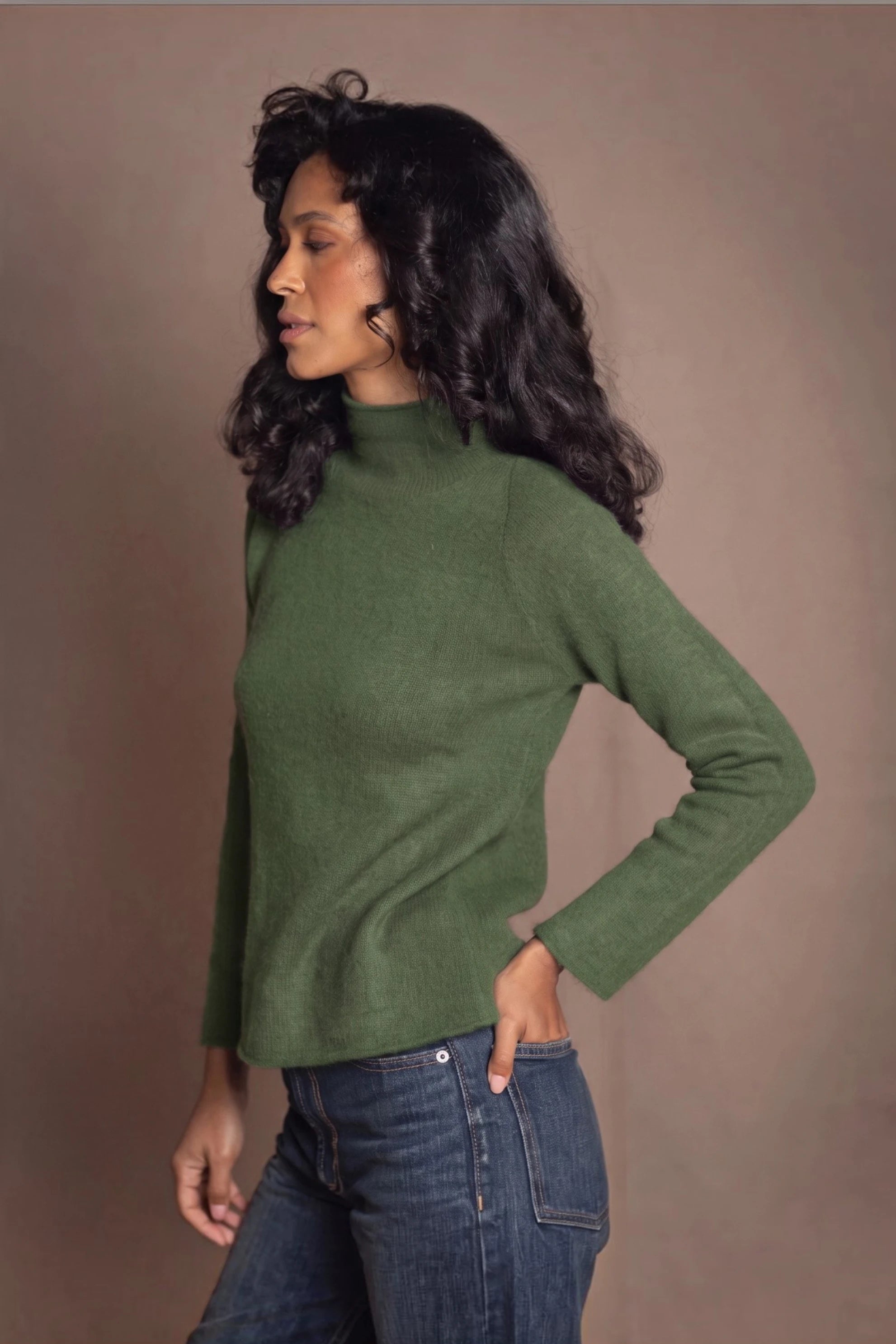 A woman wearing a green cashmere knit turtleneck sweater and dark gray silk trousers by luxury Irish Cashmere brand Madigan Cashmere