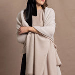 A woman wears a large cashmere shawl in beige over a matching cashmere tee