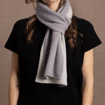 a woman wears a flannel grey two tone cashmere scarf that is reversible with white on the other side over a black cashmere tee