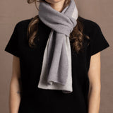 a woman wears a flannel grey two tone cashmere scarf that is reversible with white on the other side over a black cashmere tee