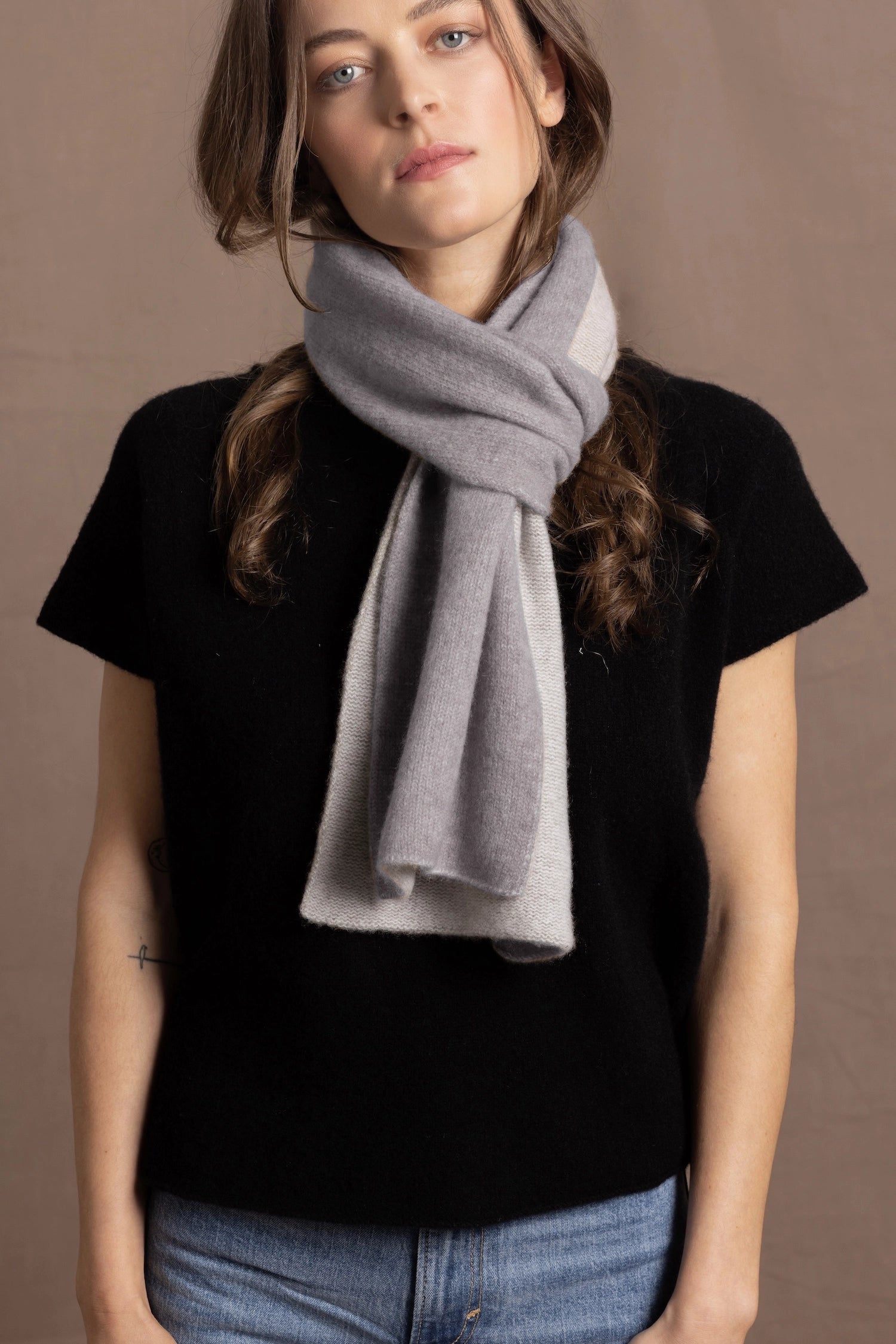 a woman wears a flannel grey two tone cashmere scarf that is reversible with white on the other side over a black cashmere tee