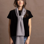 a woman wears a flannel grey two tone cashmere scarf that is reversible with white on the other side over a black cashmere tee. It goes to her hip in length