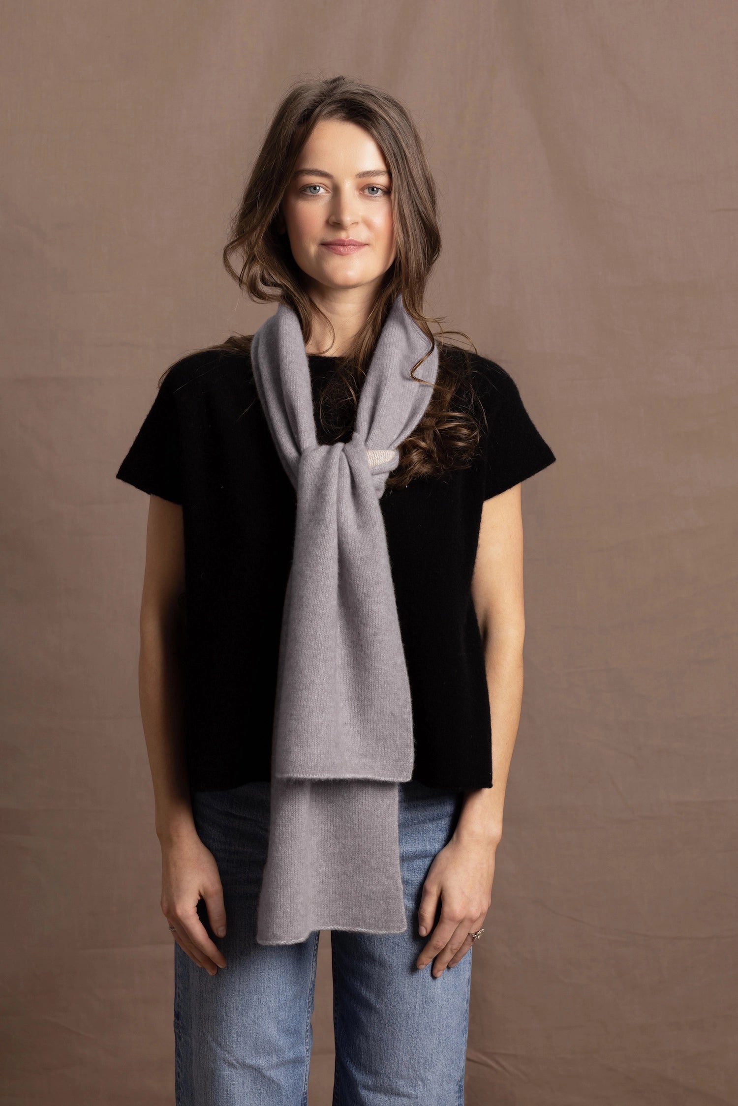 a woman wears a flannel grey two tone cashmere scarf that is reversible with white on the other side over a black cashmere tee. It goes to her hip in length