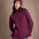 A woman wearing a burgundy cashmere turtleneck sweater, matching knit cashmere beanie, and blue jeans