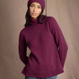 A woman wearing a burgundy cashmere turtleneck sweater, matching knit cashmere beanie, and blue jeans