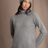 A woman wearing a light gray cashmere turtleneck sweater, matching knit cashmere beanie, and blue jeans