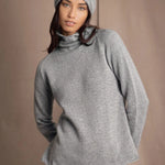 A woman wearing a light gray cashmere turtleneck sweater, matching knit cashmere beanie, and blue jeans