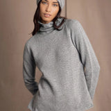 A woman wearing a light gray cashmere turtleneck sweater, matching knit cashmere beanie, and blue jeans