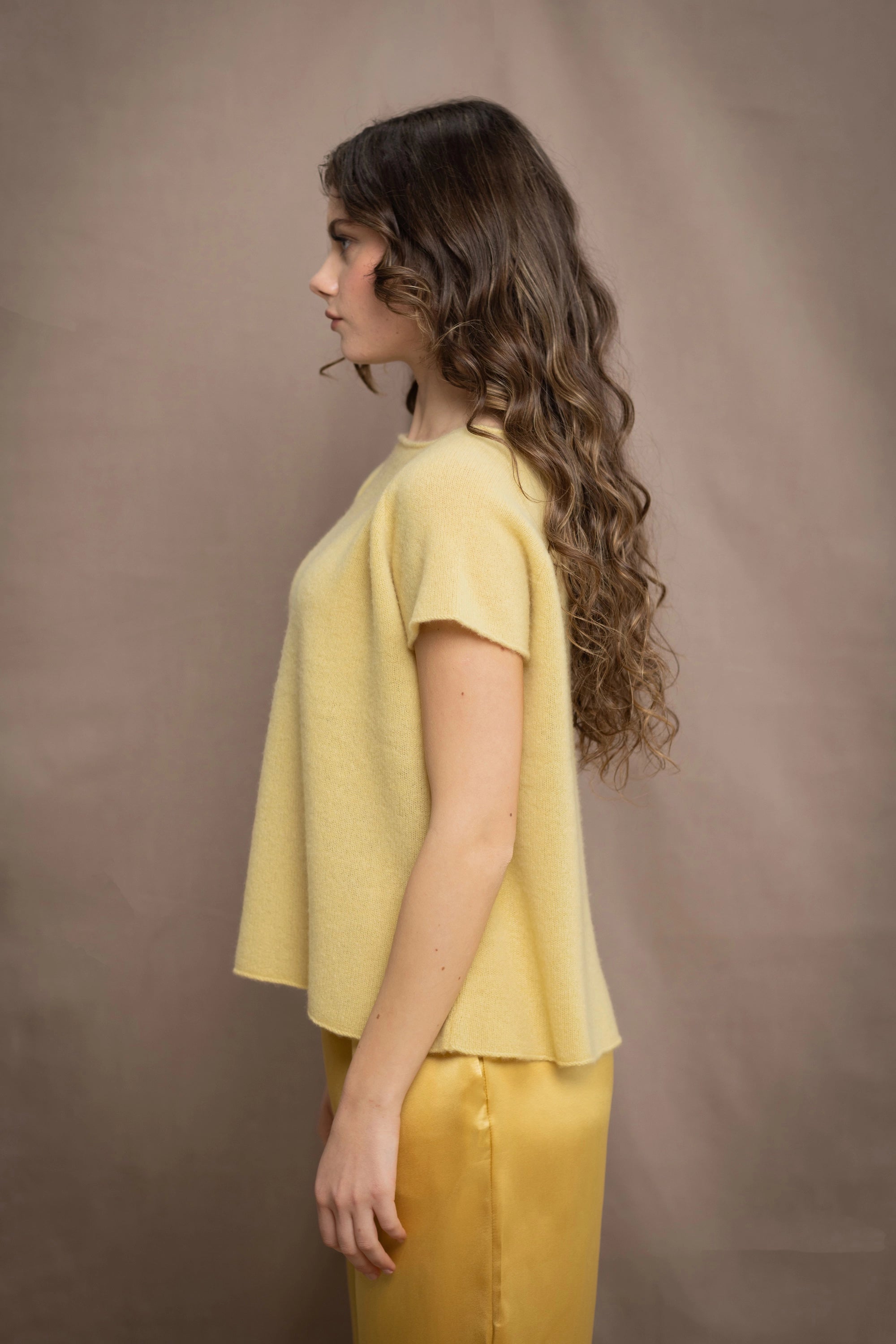 a woman wears a pure 100% cashmere tee sweater in butter yellow over silk trousers in butter yellow