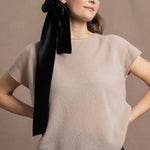 A woman wears a 100% cashmere tshirt in beige with a black silk tie in her hair and black silk shorts