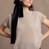 A woman wears a 100% cashmere tshirt in beige with a black silk tie in her hair and black silk shorts