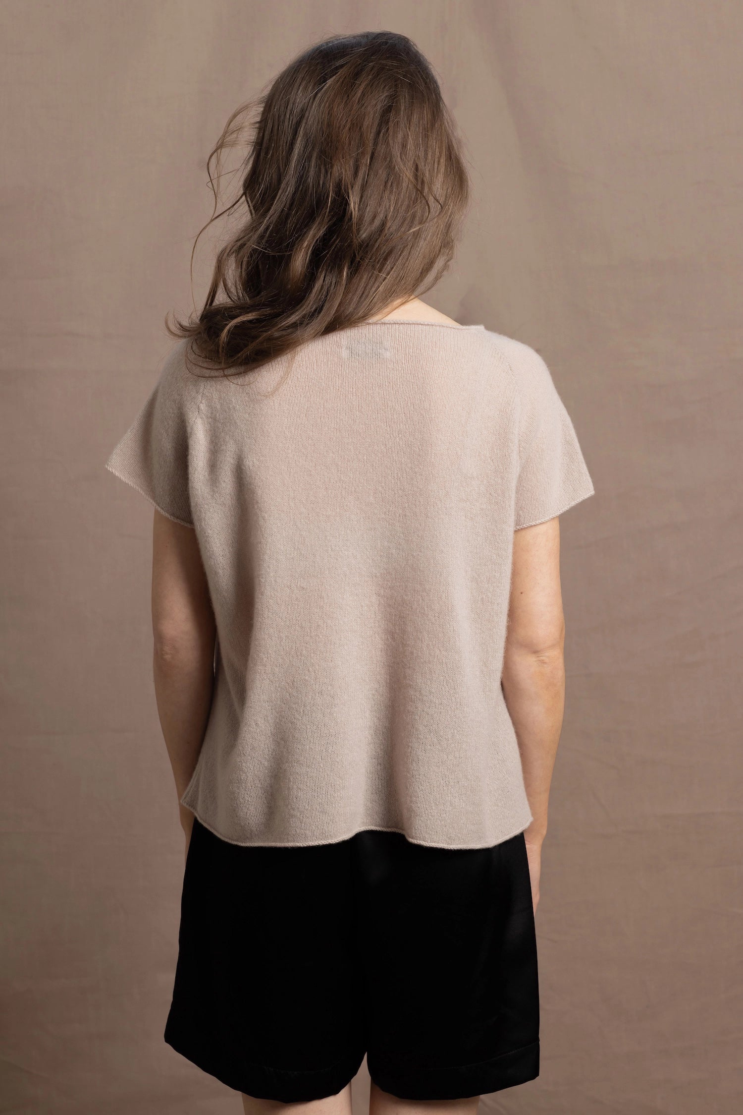 A woman wears a 100% cashmere tshirt in beige with pure silk shorts in black