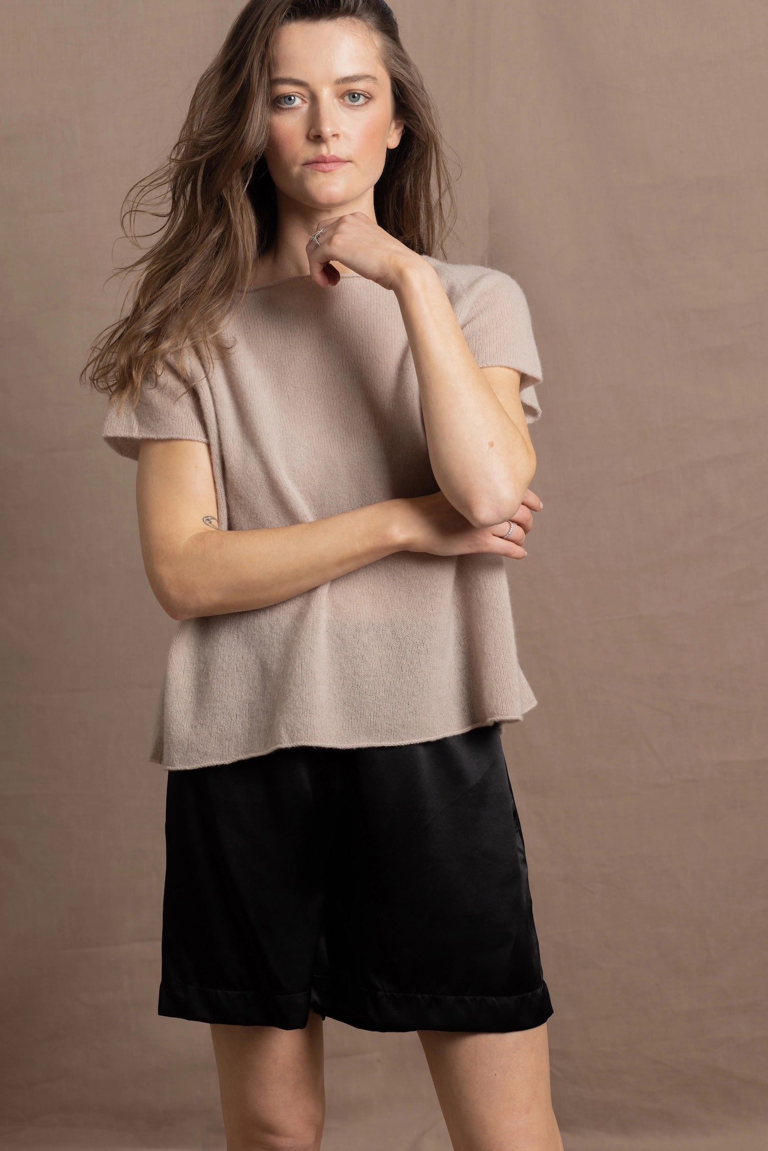 A woman wears a 100% cashmere tshirt in beige with pure silk shorts in black