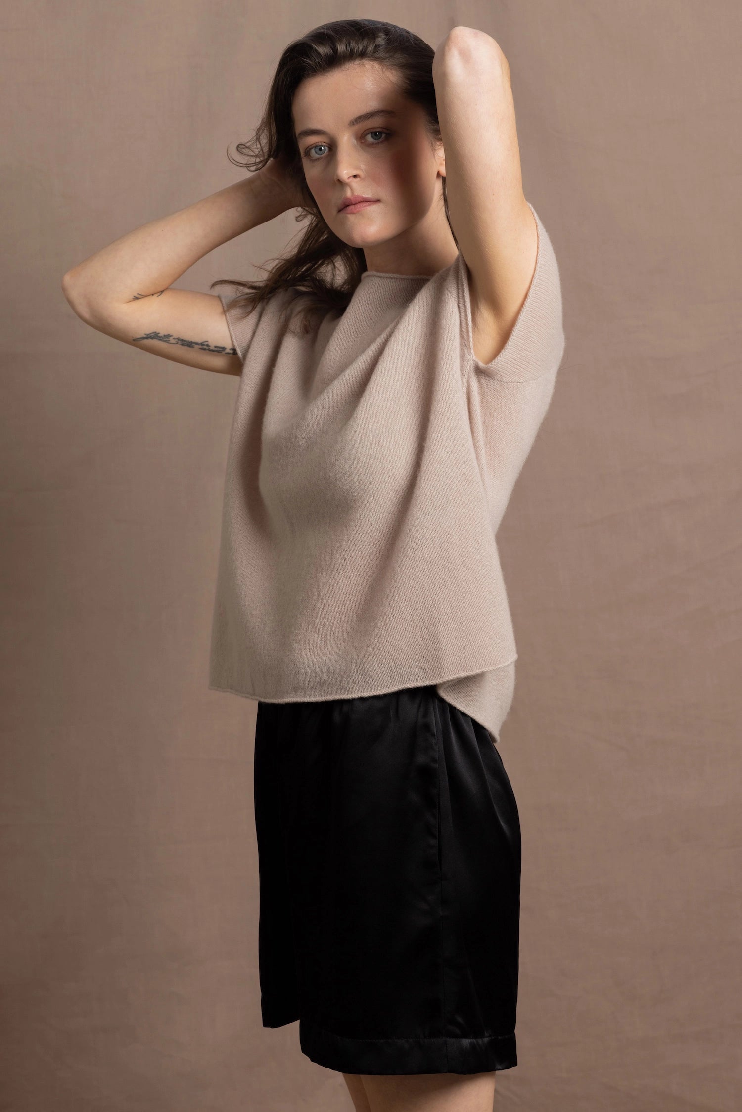 A woman wears a 100% cashmere tshirt in beige with pure silk shorts in black