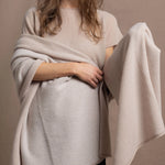 A woman wears a large cashmere shawl in beige over a matching cashmere tee