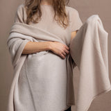 A woman wears a large cashmere shawl in beige over a matching cashmere tee