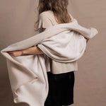 A woman wears a large cashmere shawl in beige over a matching cashmere tee and black silk shorts
