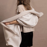 A woman wears a large cashmere shawl in beige over a matching cashmere tee and black silk shorts