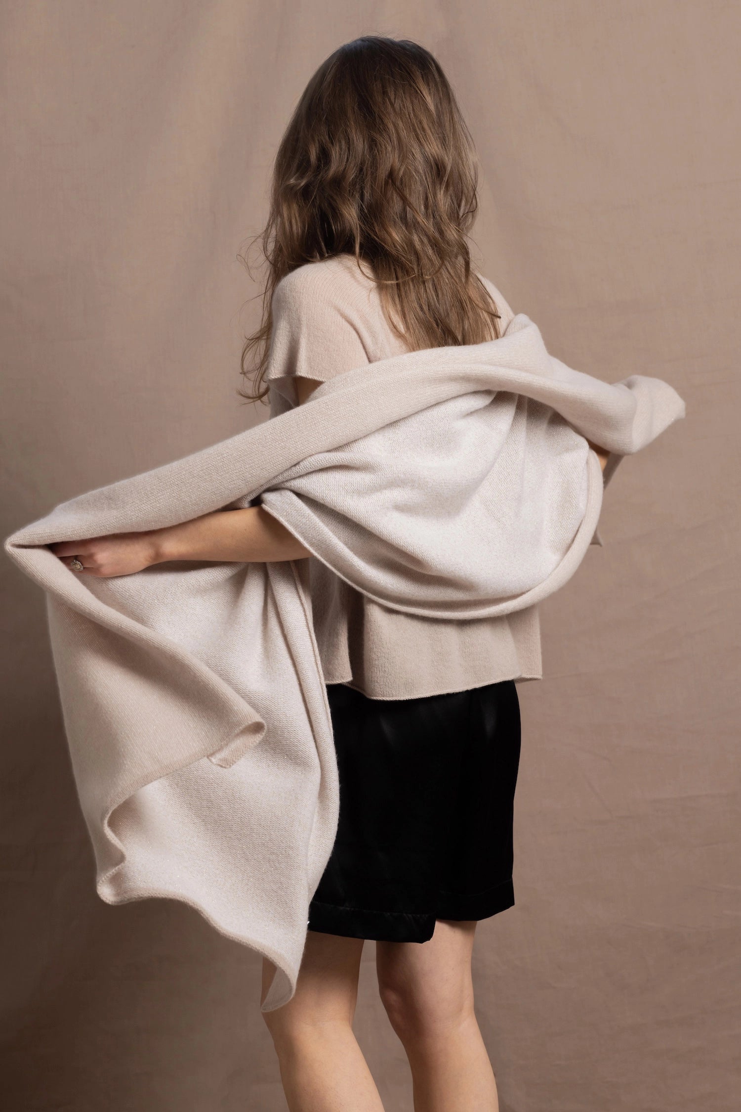 A woman wears a large cashmere shawl in beige over a matching cashmere tee and black silk shorts
