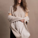 A woman wears a large cashmere shawl in beige over a matching cashmere tee