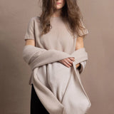 A woman wears a large cashmere shawl in beige over a matching cashmere tee