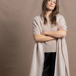 A woman wears a large cashmere shawl in beige over a matching cashmere tee and black silk shorts
