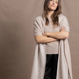 A woman wears a large cashmere shawl in beige over a matching cashmere tee and black silk shorts
