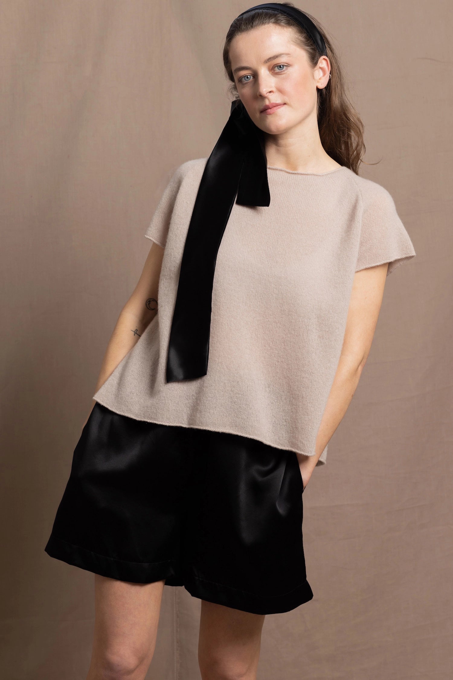 A woman wears a 100% cashmere tshirt in beige with pure silk shorts in black with a black silk tie in her hair