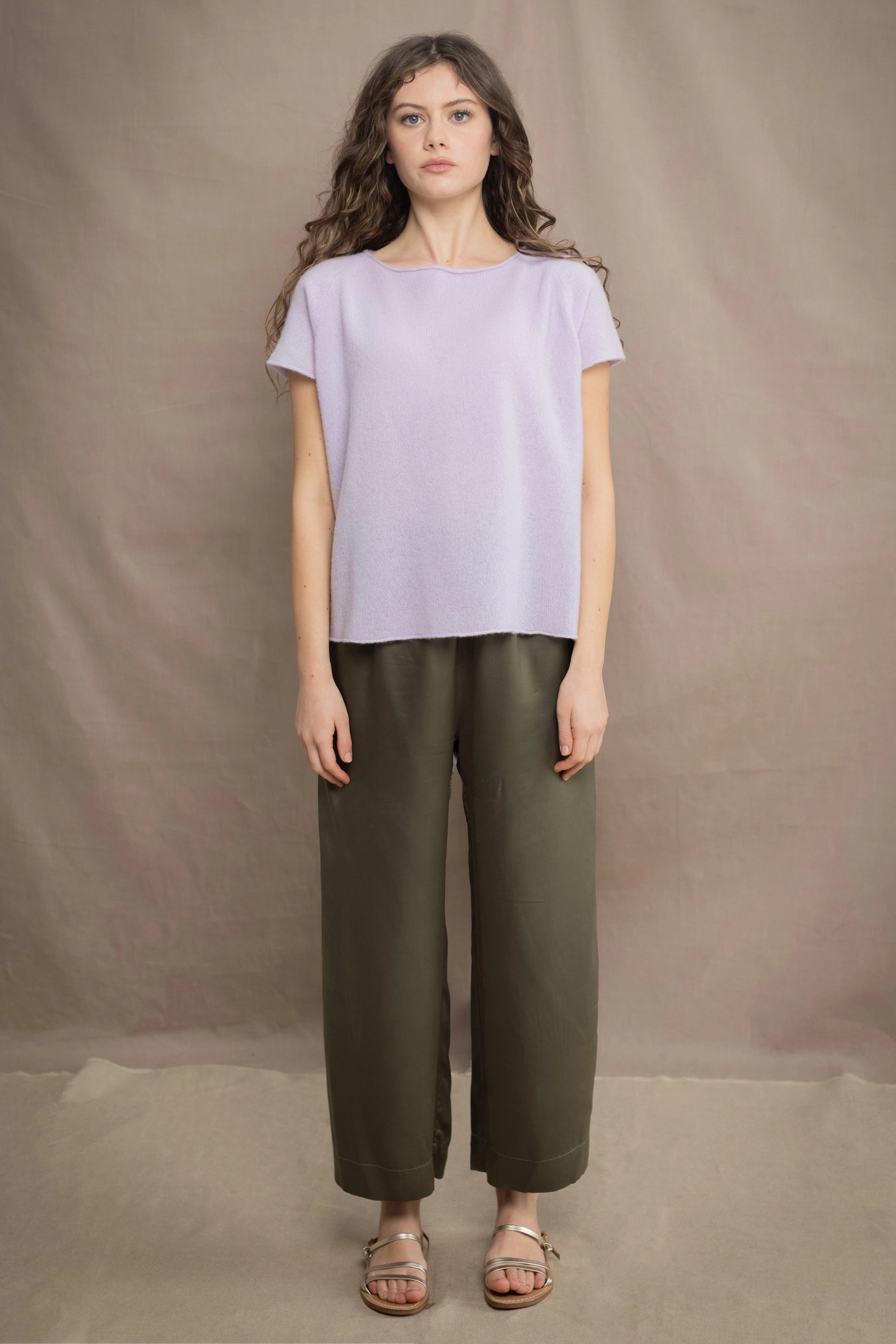 a woman wears a 100% pure cashmere tee sweater in light purple by Irish brand Madigan Cashmere with silk trousers in green