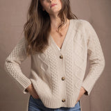 a woman wears a beige coloured cashmere aran cardigan sweater with horn buttons on it and diamond stitches